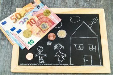 Geld auf einer Kreidetafel, auf der ein Haus gezeichnet ist. Foto: @ steidi-Fotolia.com