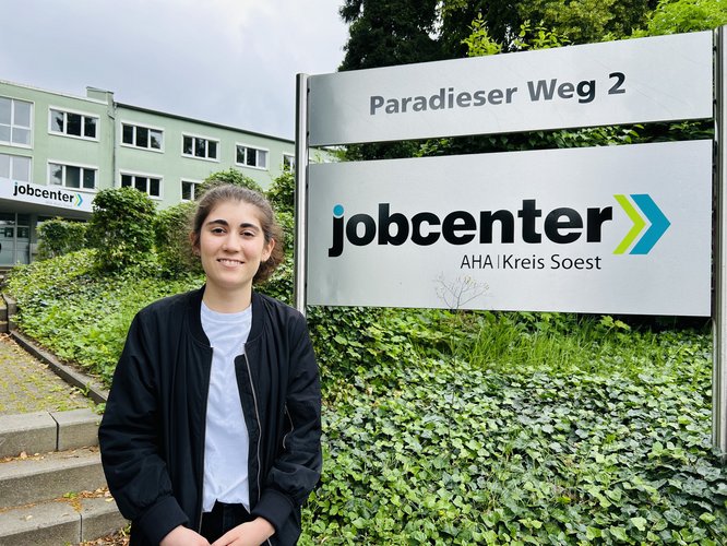 Eine junge Frau steht vor dem Schild des Jobcenters AHA in Soest.