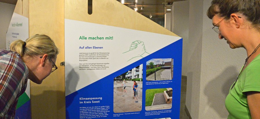 Bei Personen betrachten den Aufsteller zur Ausstellung „Aufgepasst. Angepasst!“. Foto: Kira Hönicke/ Kreis Soest