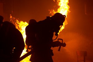 Die schwarze Silhouette eines Feuerwehrmanns direkt vor einem Feuer. Foto: Dirk Behrens/Kreis Soest
