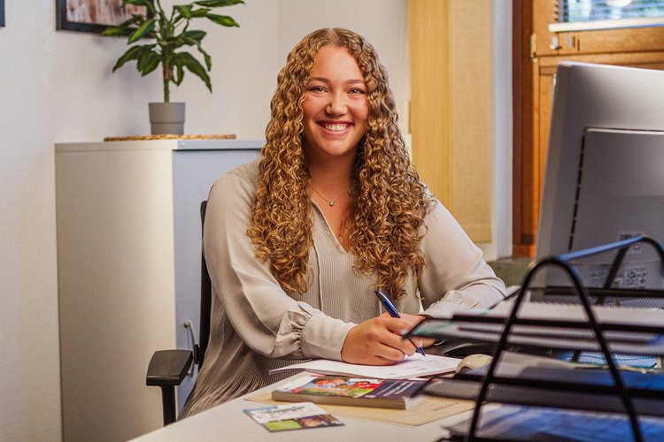 Eine Frau sitzt lächelnd an ihrem Arbeitsplatz. Foto: Thomas Grimm